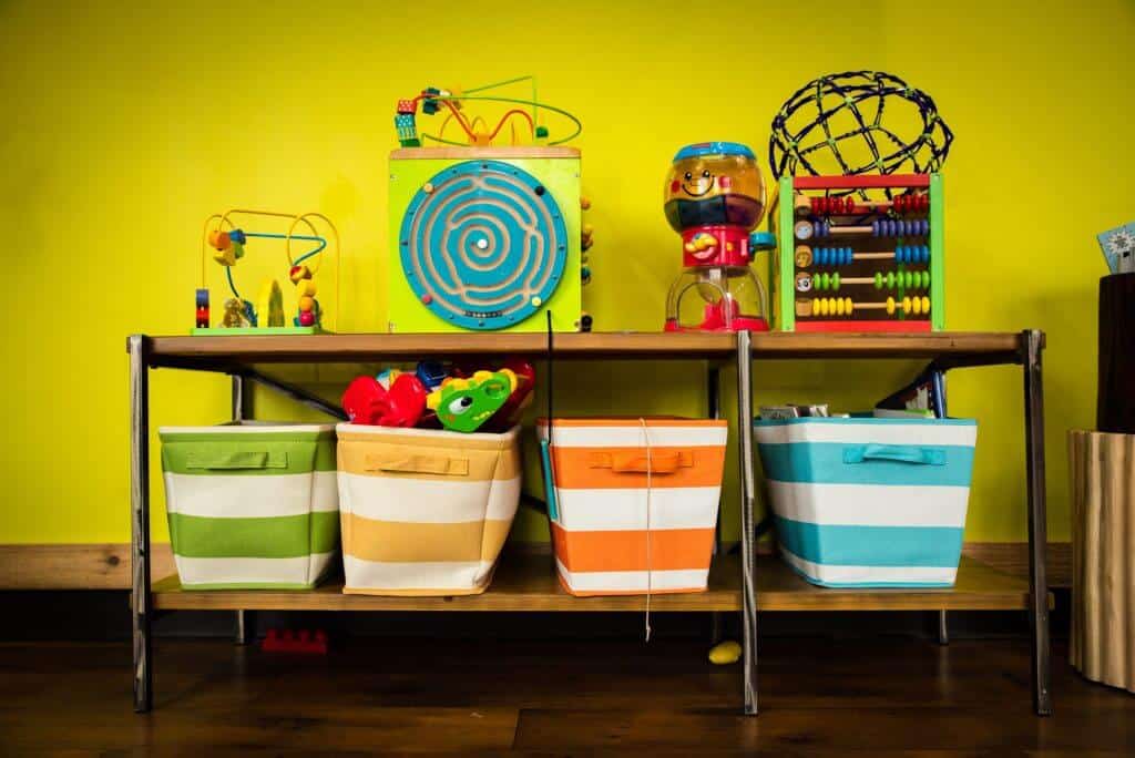 a rack with striped design colored bins and activities and toys against a colored bright yellow wall 